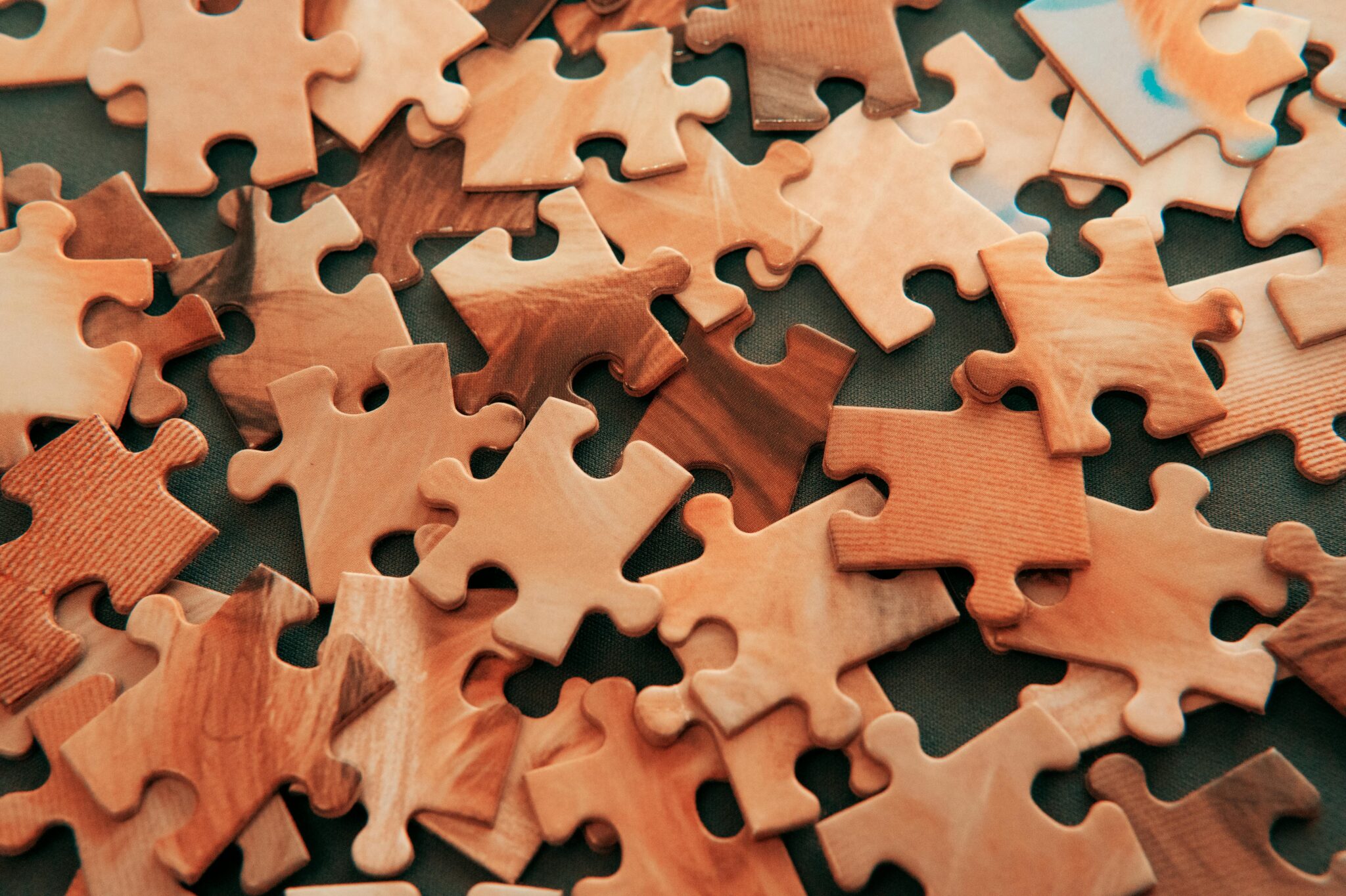 A close-up view of scattered wooden jigsaw puzzle pieces on a dark surface.